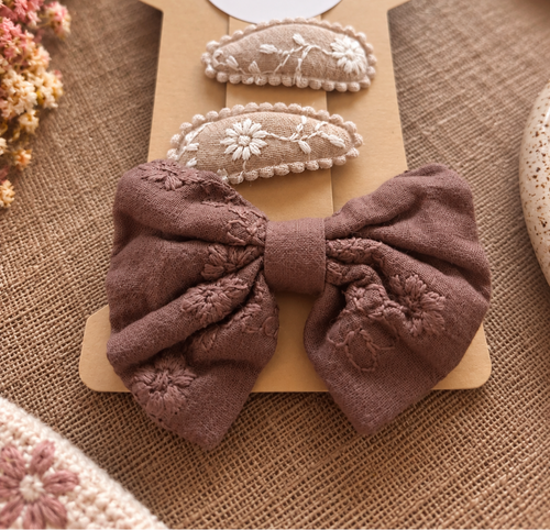 Close-up Cocoa Lace beige bloemspeldjes en warmbruine geborduurde strik