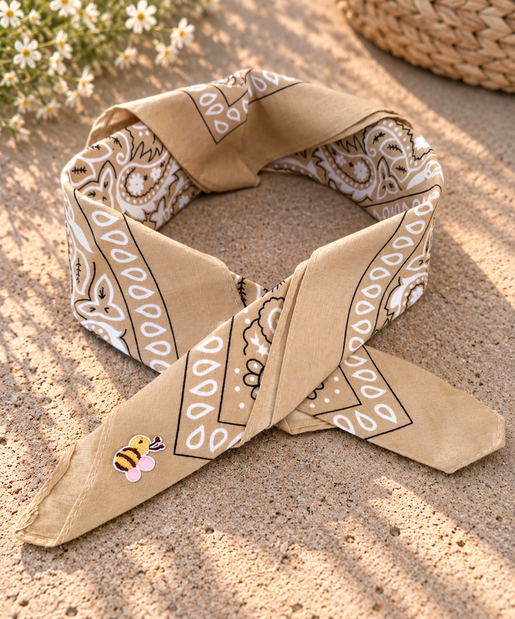 Desert Honey Bee kinderbandana in zandkleurige paisley, opgevouwen met een embleem van een bijtje op de punt