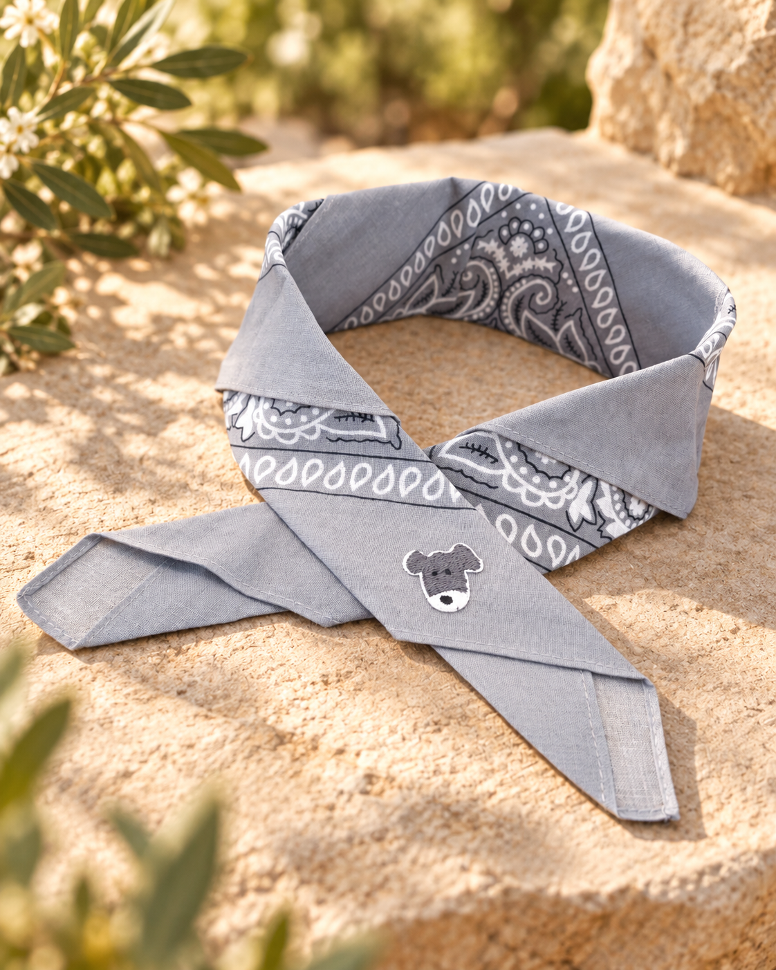 Doggy Grey kinderbandana in grijze paisley, opgevouwen met een embleem van een grijs-wit hondje op de punt