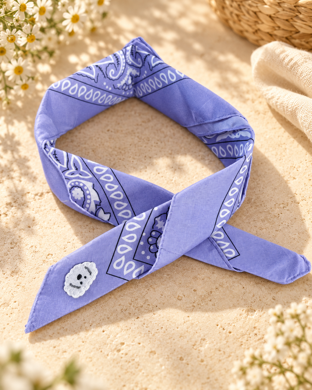 Doggy Lilac kinderbandana in lila paisley, opgevouwen met een embleem van een wit hondje op de punt
