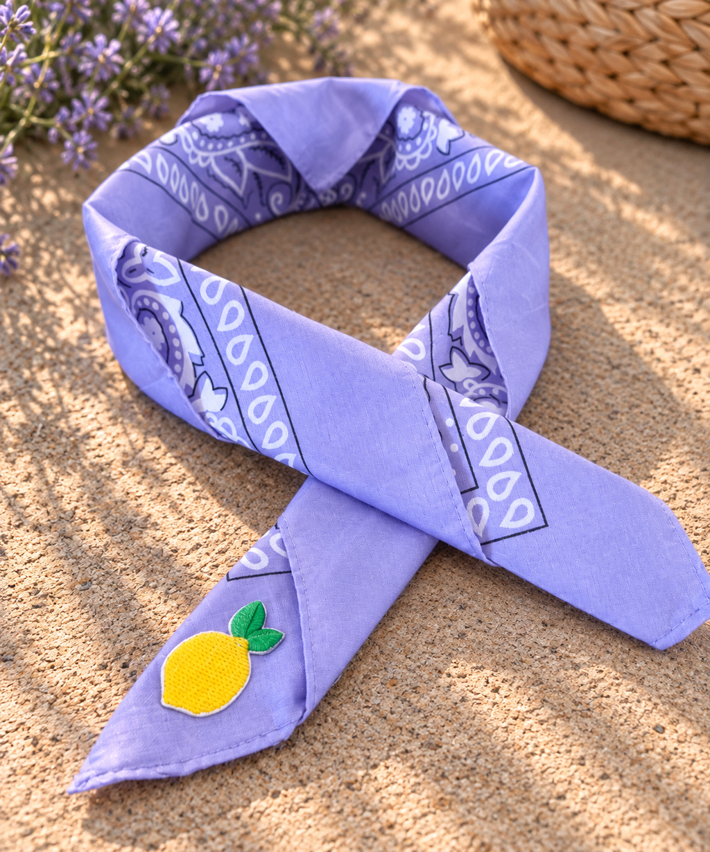 Lemon Lilac kinderbandana in lila paisley, opgevouwen met een embleem van een gele citroen op de punt