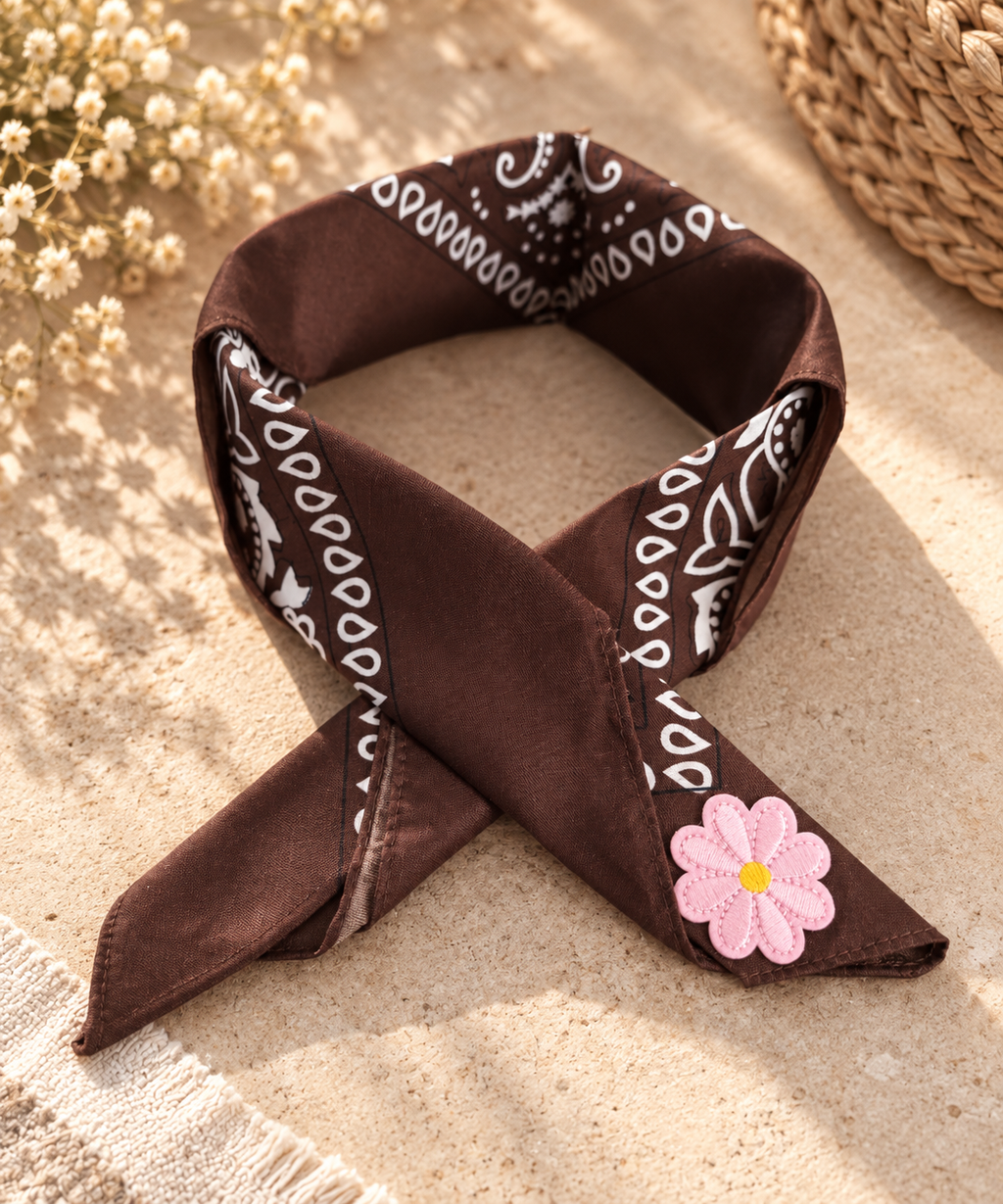 Pink Daisy Brown kinderbandana in chocoladebruine paisley, opgevouwen met een embleem van een roze bloem op de punt