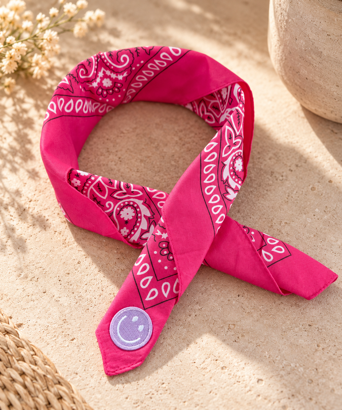 Smiley Fuchsia kinderbandana in fuchsia paisley, opgevouwen met een embleem van een lila smiley op de punt