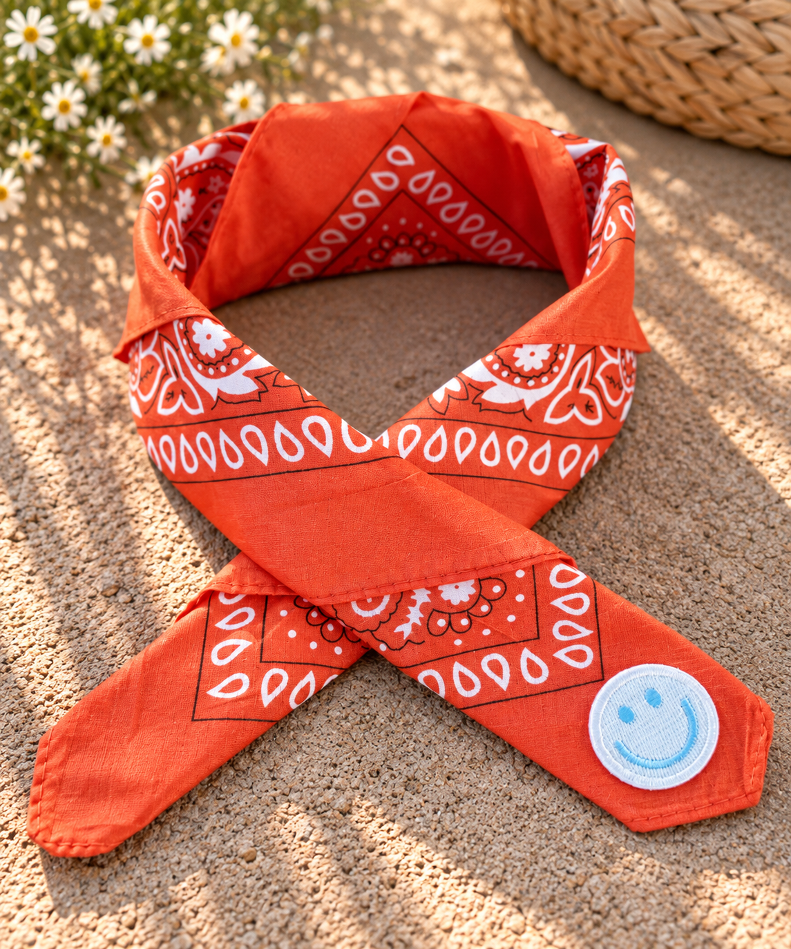 Smiley Orange kinderbandana in oranje paisley, opgevouwen met een embleem van een lichtblauwe smiley op de punt
