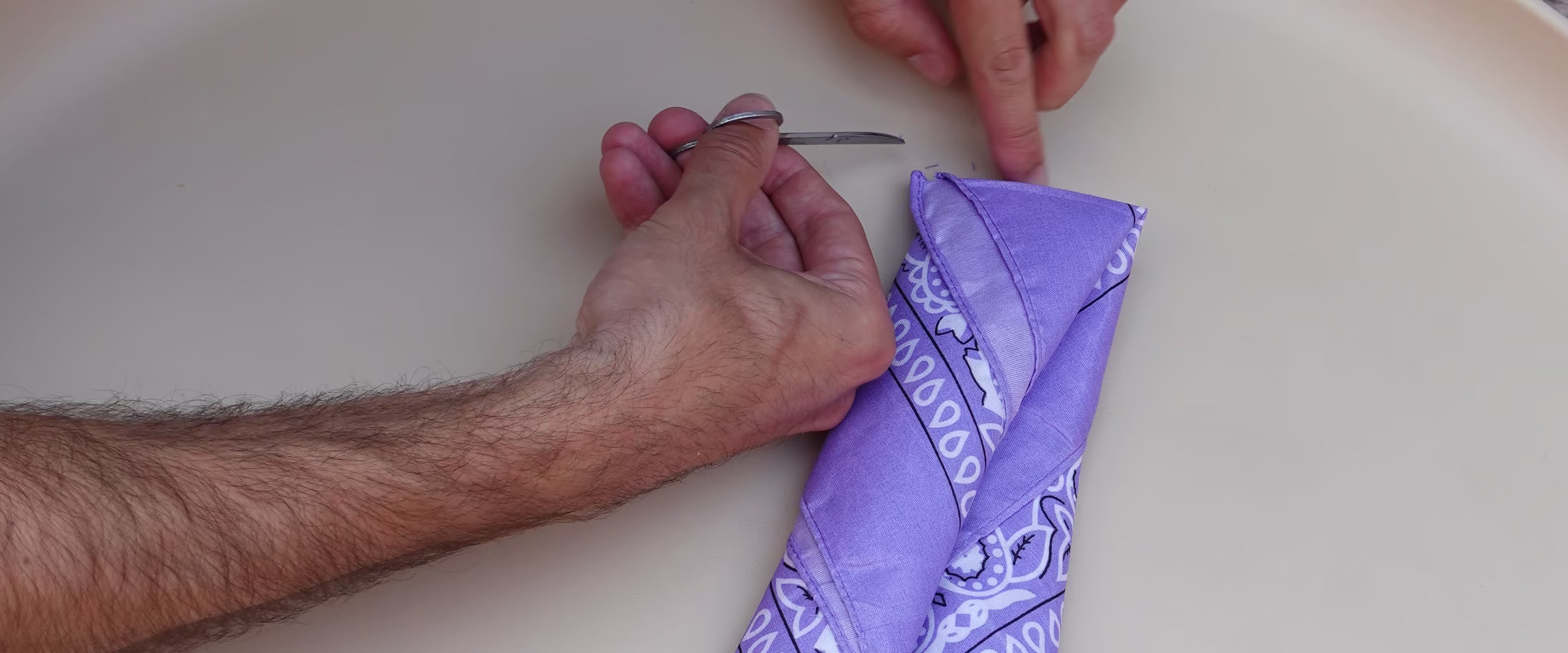 Handen controleren de afwerking van een paarse Tiny Ties bandana
