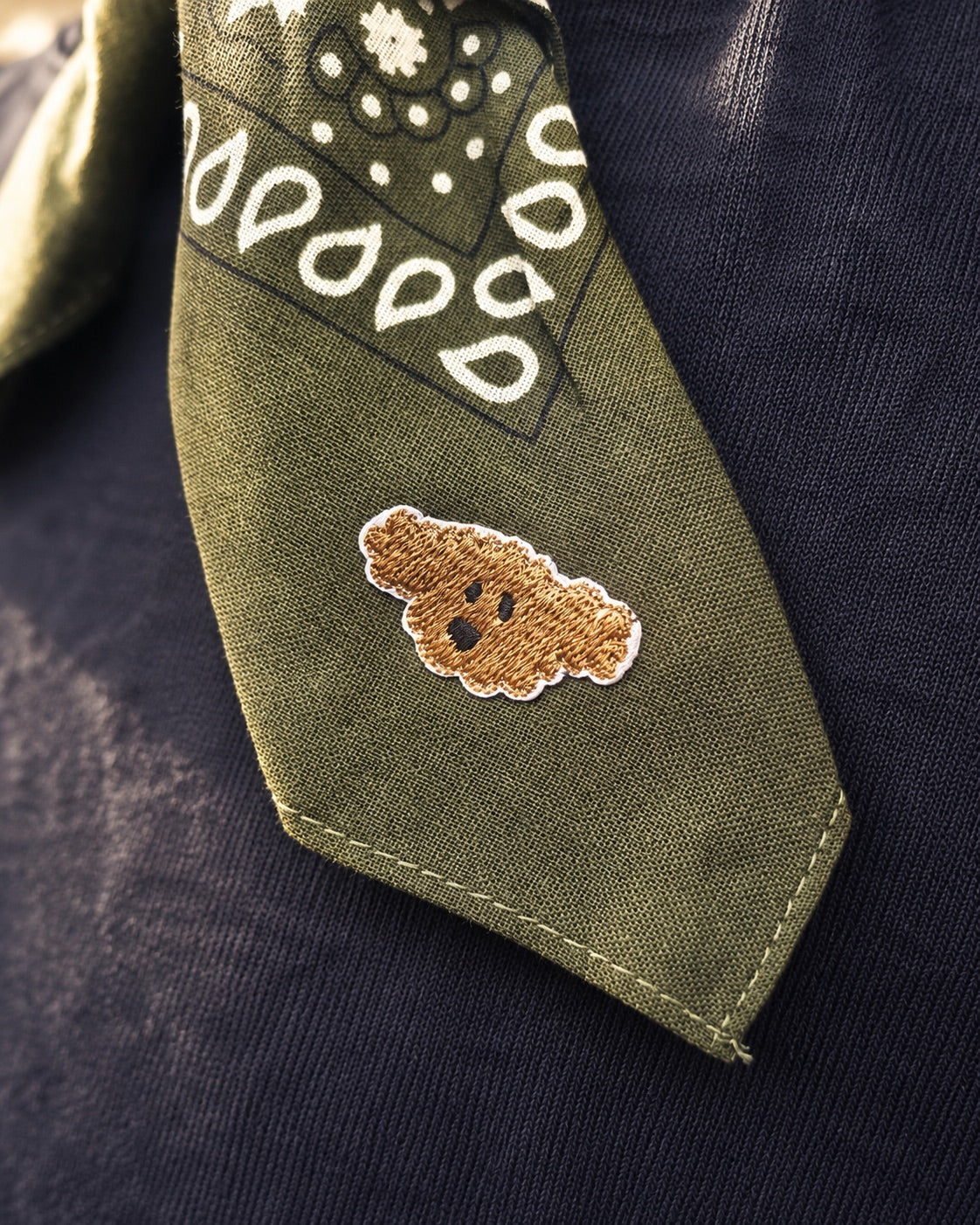 Close-up van groene Tiny Ties bandana met teddy-strijkembleem en doorgestikte zoom