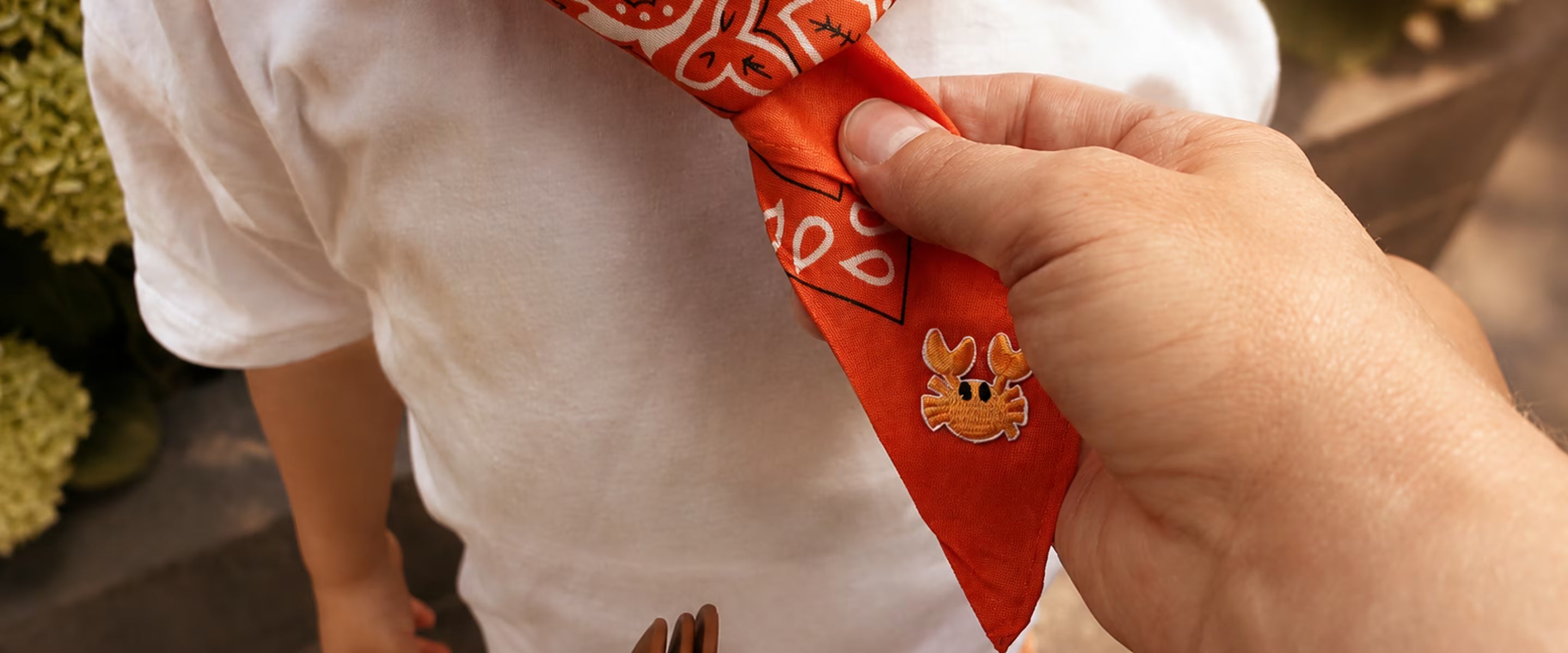 Oranje Tiny Ties bandana met krab-embleem wordt bij een kind omgeknoopt