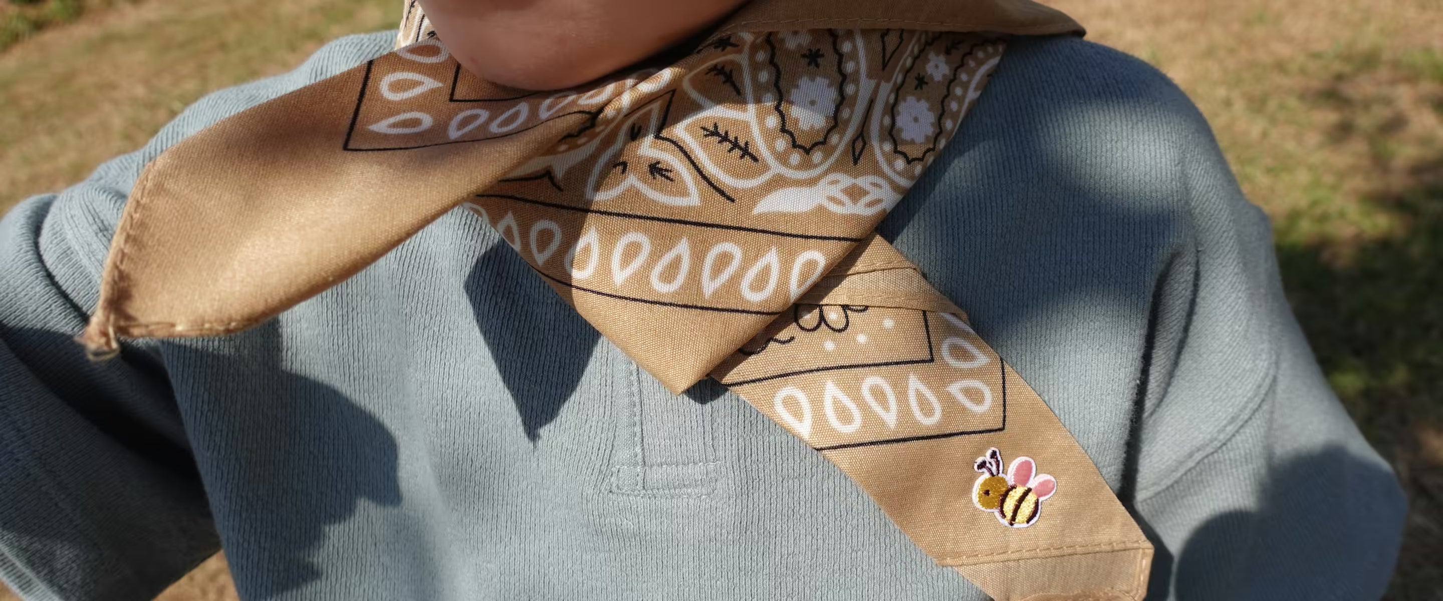 Kind draagt buiten een zandkleurige Tiny Ties bandana met bijen-embleem