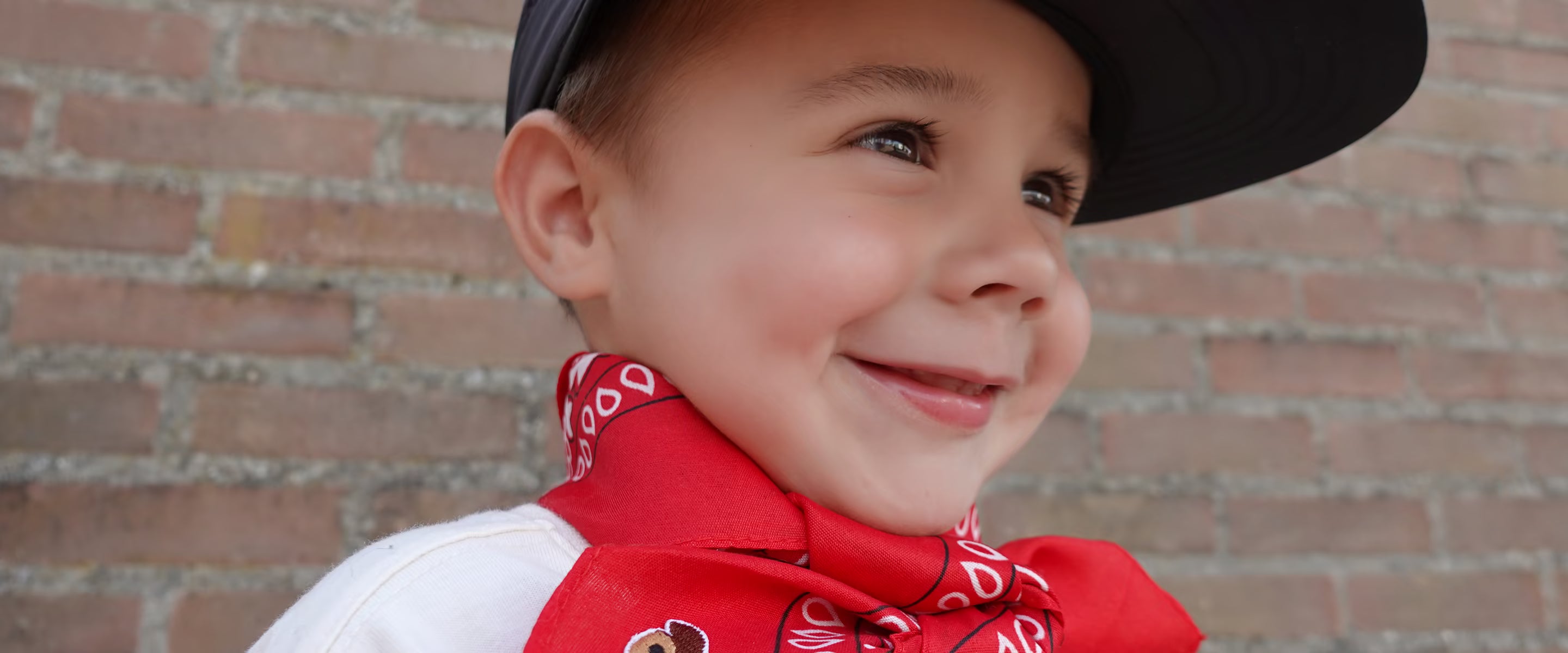 Kind draagt een rode Tiny Ties bandana met teddy-embleem om de nek