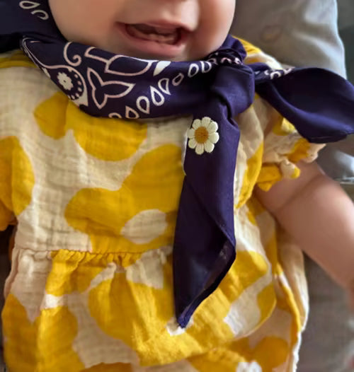 Baby draagt een donkerpaarse Tiny Ties bandana met bloem-embleem, klantfoto bij de Google review van Lotte v.b